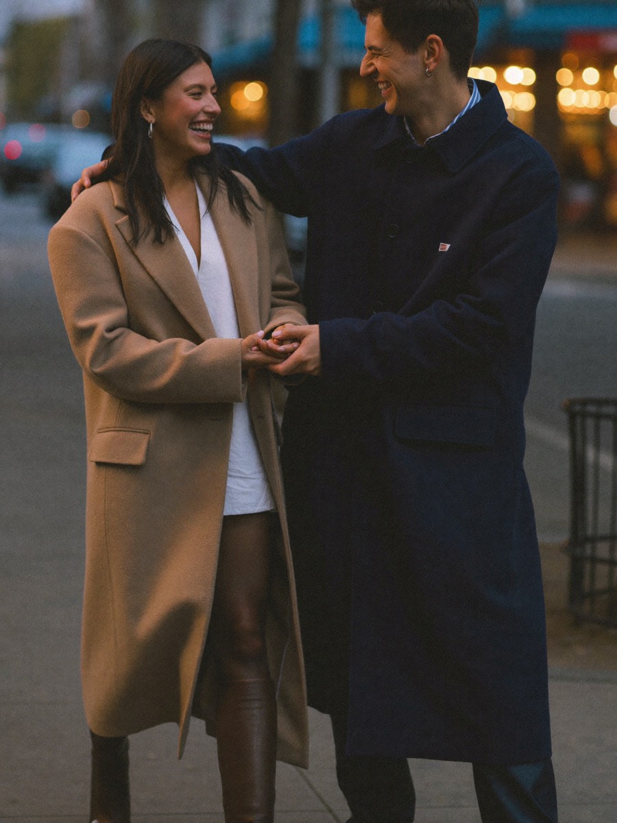 An engaged couple laughing on a city sidewalk at dusk