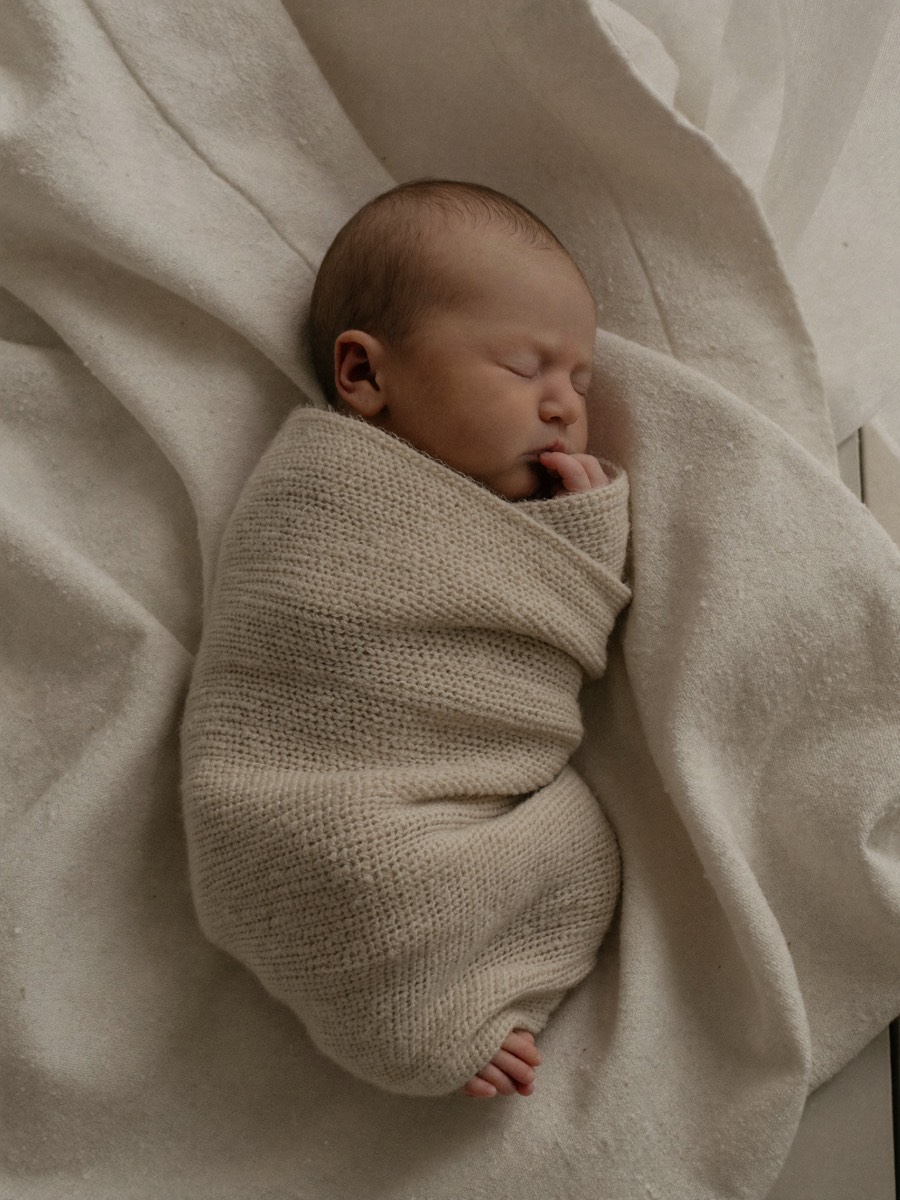 A newborn asleep in an oatmeal knit wrap
