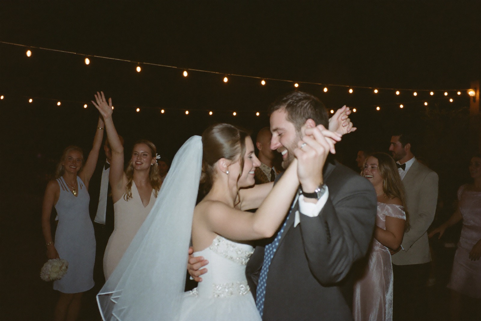 Bride and groom dancing with guests under string lights